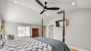 Quarto com cama, ventoinha no teto, cômoda, TV fixada na parede e janela com persianas.
