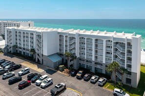 A multi-story hotel with a parking lot in front, located near a beach with clear blue waters.