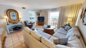 A living room with a sofa, a television, a dining table, and a balcony with curtains.