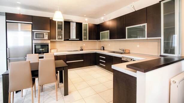 A modern kitchen with dark cabinetry, a stainless steel refrigerator, a microwave, and a dining area with a table and chairs. - Meteora's Secret Garden House 2 (Kalabaka)