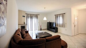 A modern living room with a brown sofa set, a flat-screen TV, a fireplace, and a dining area with a coffee table. - Meteora's Secret Garden House 2 (Kalabaka)