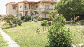 A two-story building with a stone staircase leading to a balcony, surrounded by well-maintained gardens and a paved pathway. - Meteora's Secret Garden House 2 (Kalabaka)