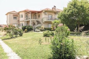 A two-story building with a stone staircase leading to a balcony, surrounded by well-maintained gardens and a paved pathway.
