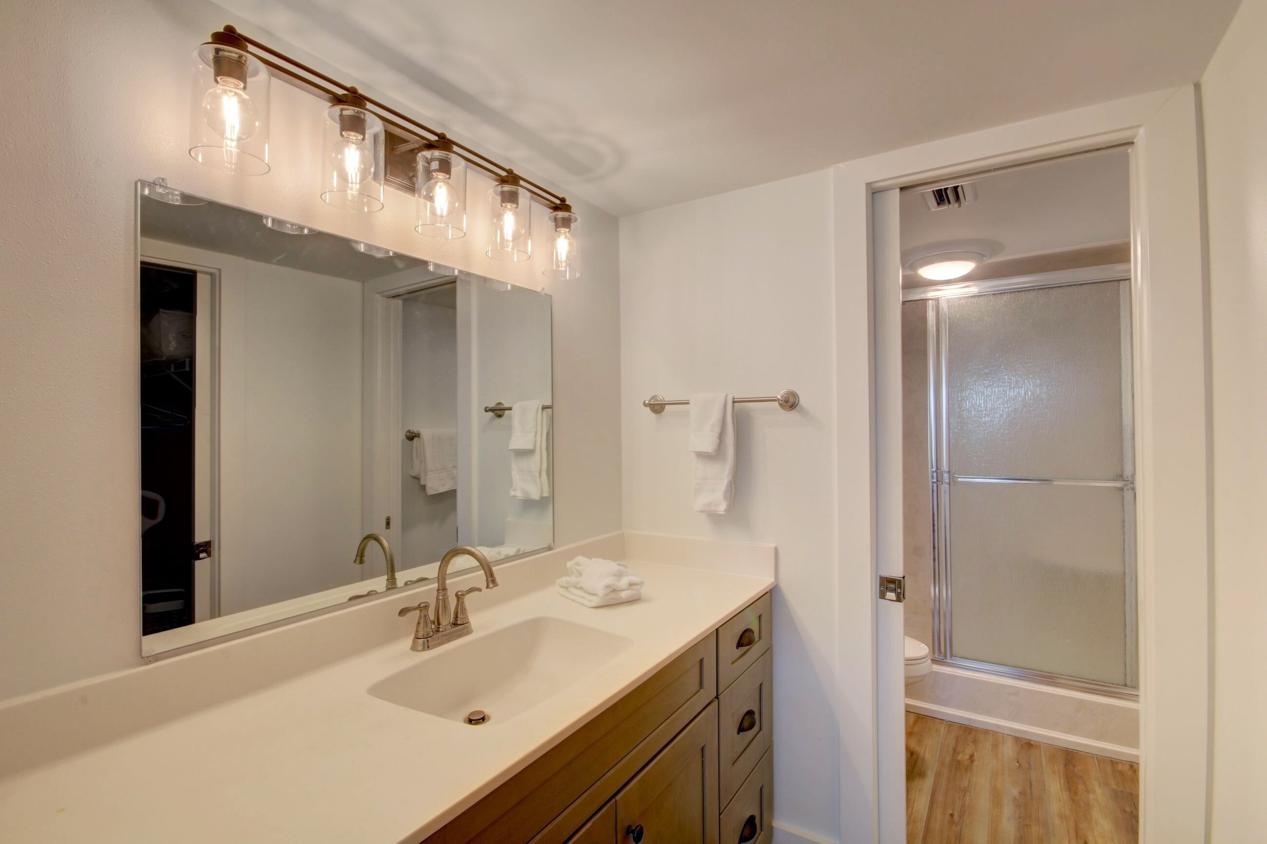 A bathroom with a large mirror, a sink, a towel rack, and a glass-enclosed shower.