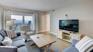 A modern living room with a sofa, armchair, and coffee table. A flat-screen TV is mounted on the wall, and there is a wooden cabinet below it.