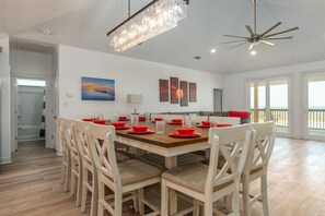 Un comedor amplio con una gran mesa de madera dispuesta para seis comensales, sillas blancas y una lámpara de araña moderna.