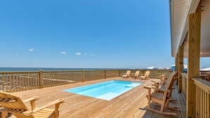Eine Holzterrasse mit Pool, Liegestühlen und Blick auf den Ozean.