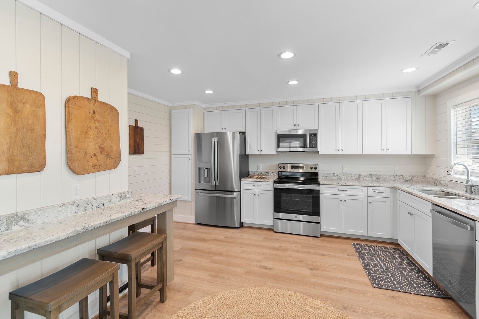 A modern kitchen with white cabinetry, stainless steel appliances, and a wooden bench.