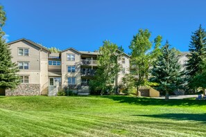 A multi-story residential building with a stone facade, a grassy lawn, and mature trees. - River Pines C207 2 Bedroom Condo by RedAwning (Edwards)
