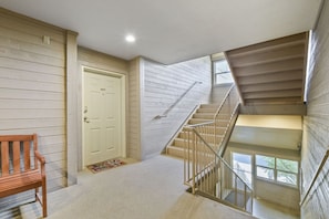 Una escalera que lleva a un piso superior, un banco de madera y una puerta blanca con el número 207.