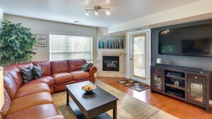 A living room with a leather sofa, a coffee table, a fireplace, a television, and a large window with blinds. - River Pines C207 2 Bedroom Condo by RedAwning (Edwards)