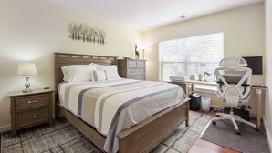 Un dormitorio con cama, mesita de noche, lámpara, escritorio, silla y ventana con persianas.