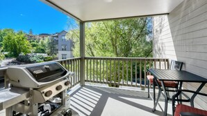 Un balcón con parrilla, mesa y sillas, con vista a una zona residencial con árboles y edificios.