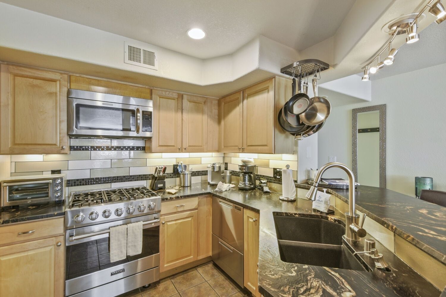 A modern kitchen with stainless steel appliances, wooden cabinets, and a marble countertop.