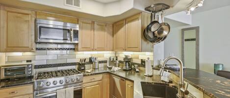 A modern kitchen with stainless steel appliances, wooden cabinets, and a marble countertop.