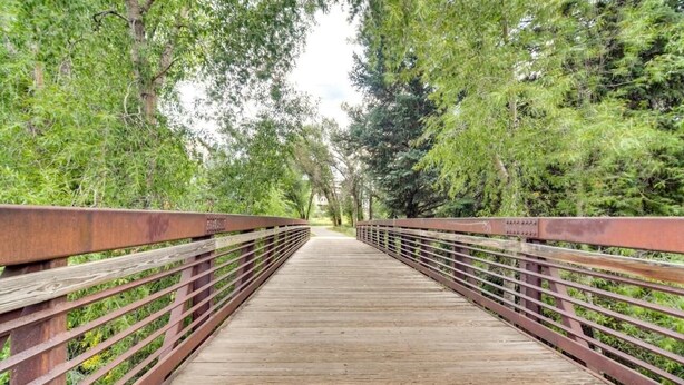 Un puente peatonal de madera con barandillas metálicas, rodeado de frondosa vegetación verde.