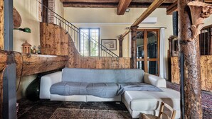 Une pièce confortable avec un canapé, un fauteuil, un escalier et une grande fenêtre.