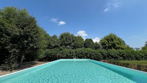 Une piscine rectangulaire à l’eau d’un bleu limpide, entourée d’arbres verdoyants et sous un ciel d’un bleu éclatant.