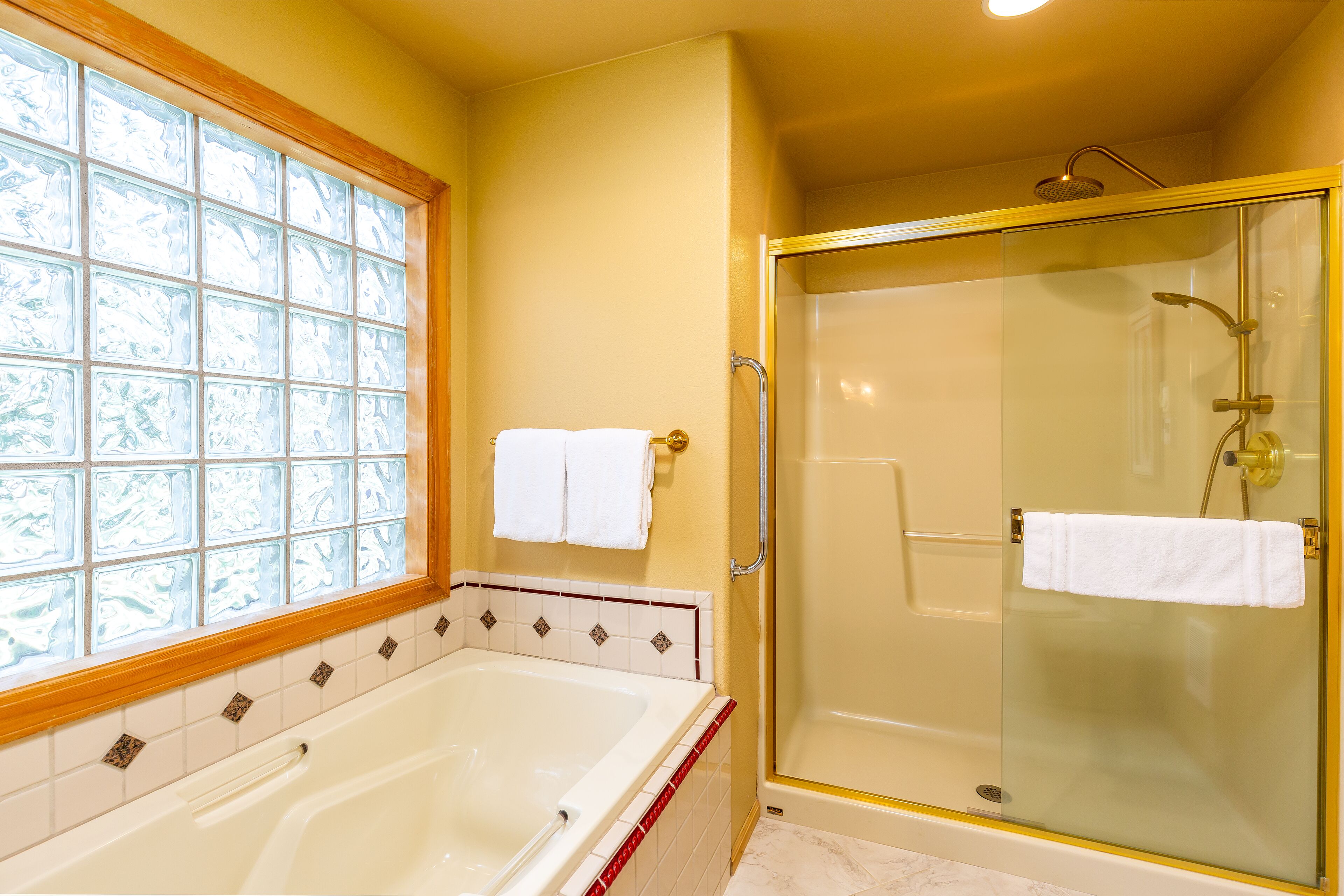 Une salle de bain dotée d’une douche à parois de verre, d’une baignoire et d’une fenêtre ornée de carreaux décoratifs.