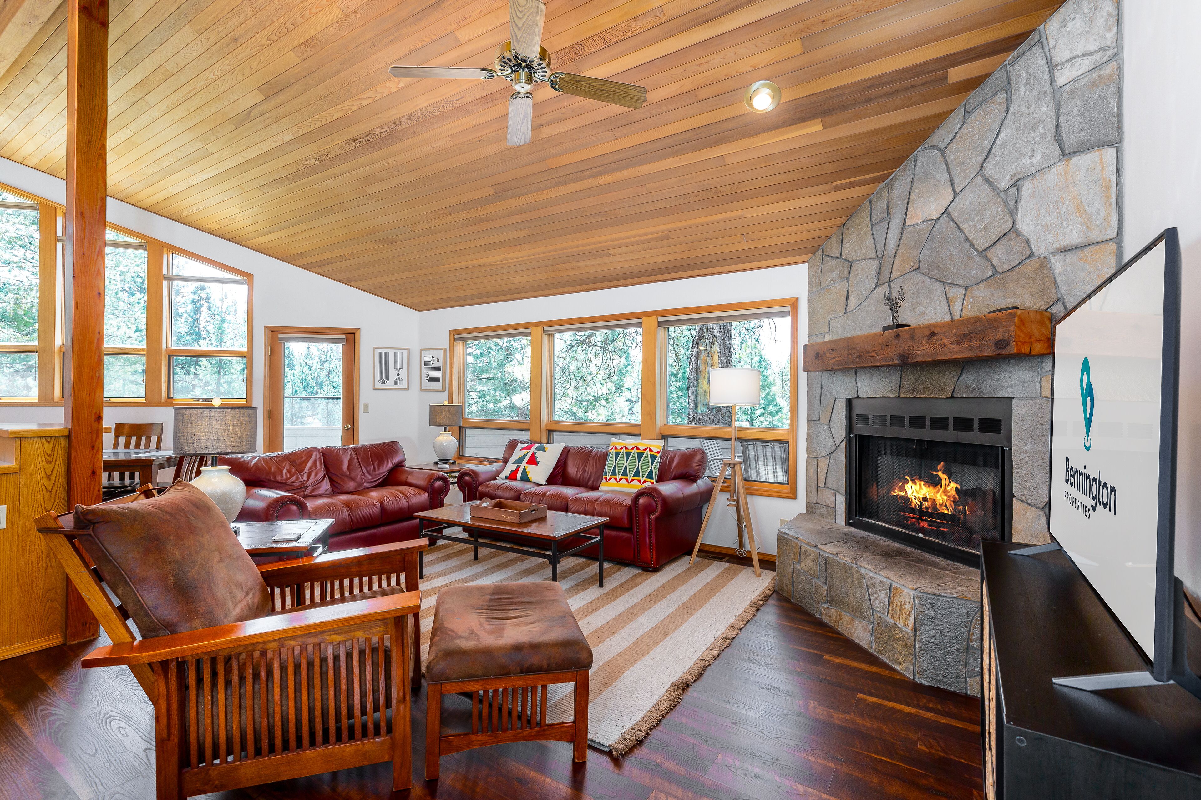 A spacious living room with a stone fireplace, leather furniture, and large windows.