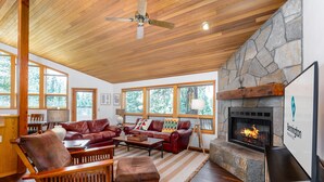 A spacious living room with a stone fireplace, leather furniture, and large windows. - MCNA33 - Spacious Home with Great Views, AC, Hot Tub (Sunriver)