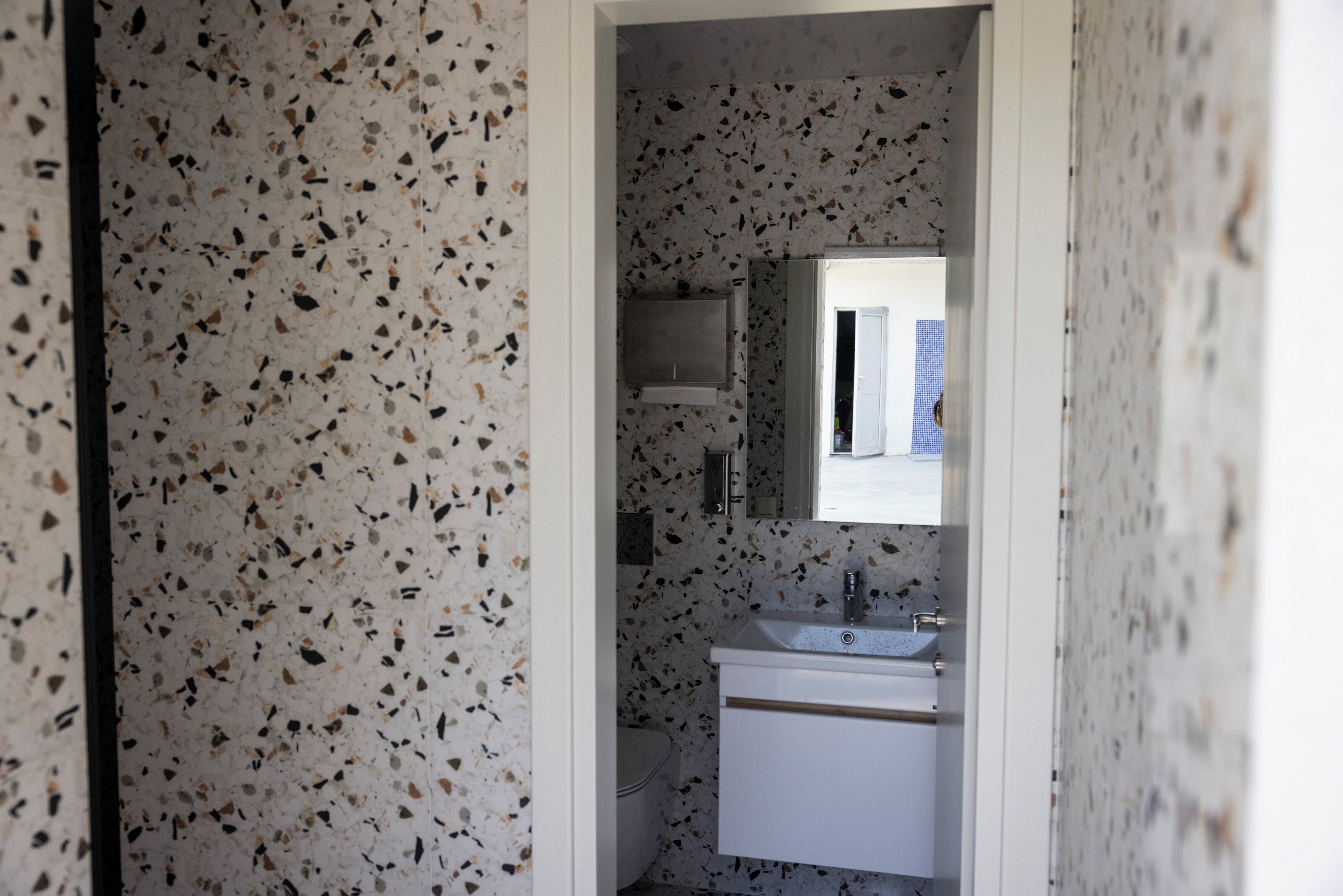 Un bany amb una paret de rajoles amb motius, un lavabo blanc i un mirall a sobre.