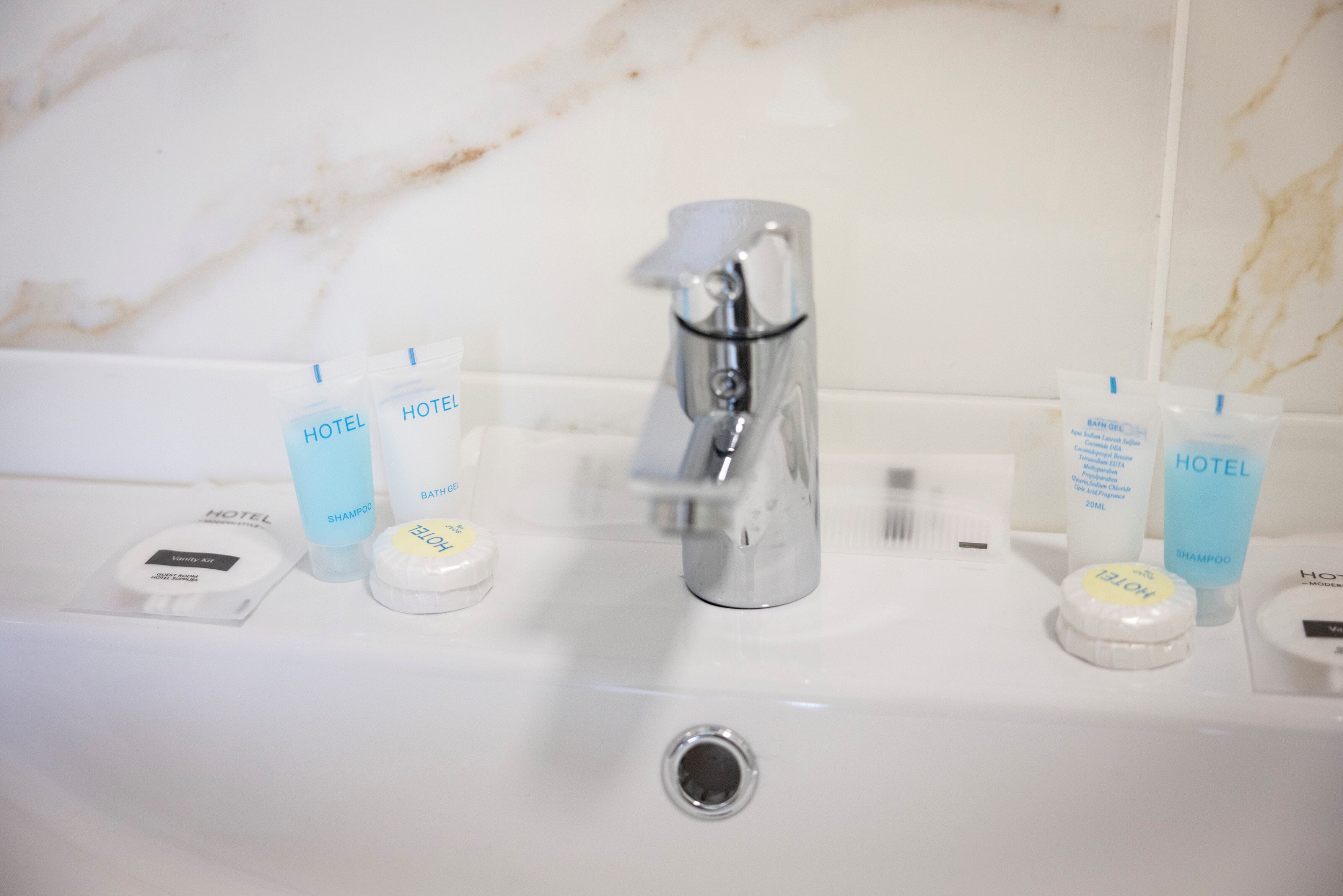 Un lavabo de salle de bain avec des articles de toilette d’hôtel, notamment du shampoing et du gel douche.