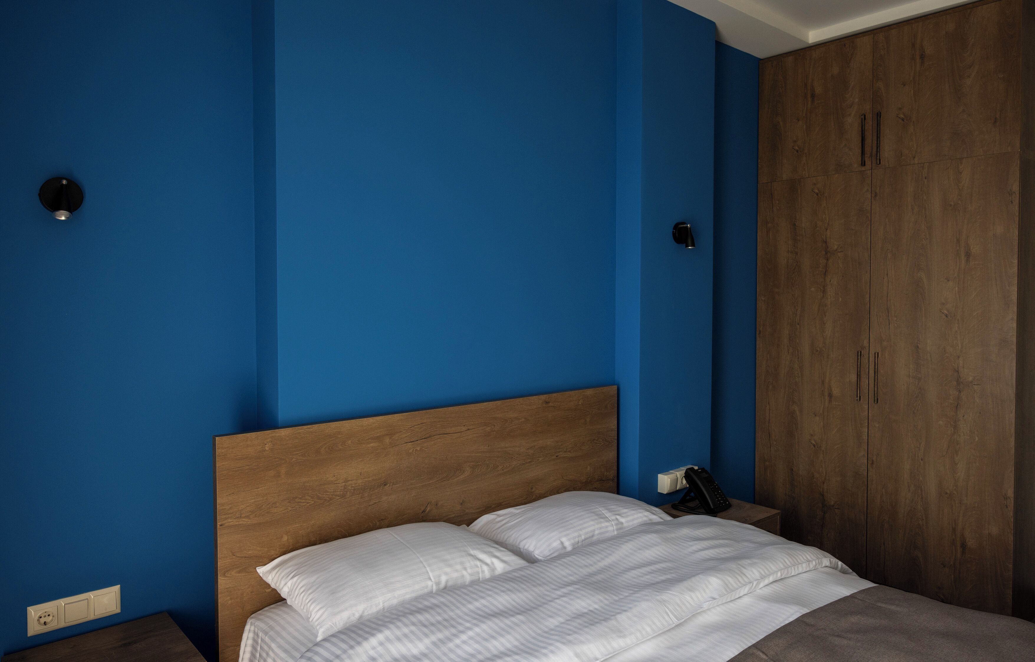 A bedroom with a wooden headboard, a bed with white linens, a wardrobe, and a bedside table with a phone.