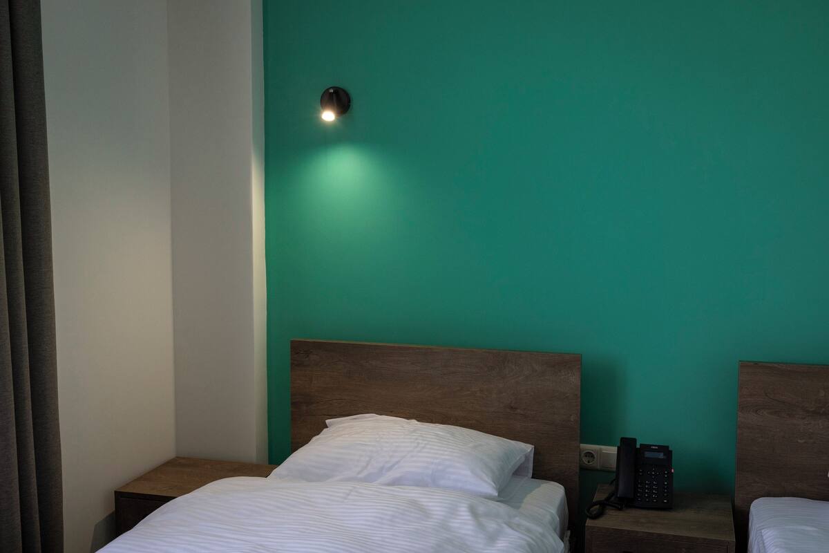 Habitación de hotel con pared verde azulado, cabecera de madera, teléfono en la mesita de noche y mesita de noche.