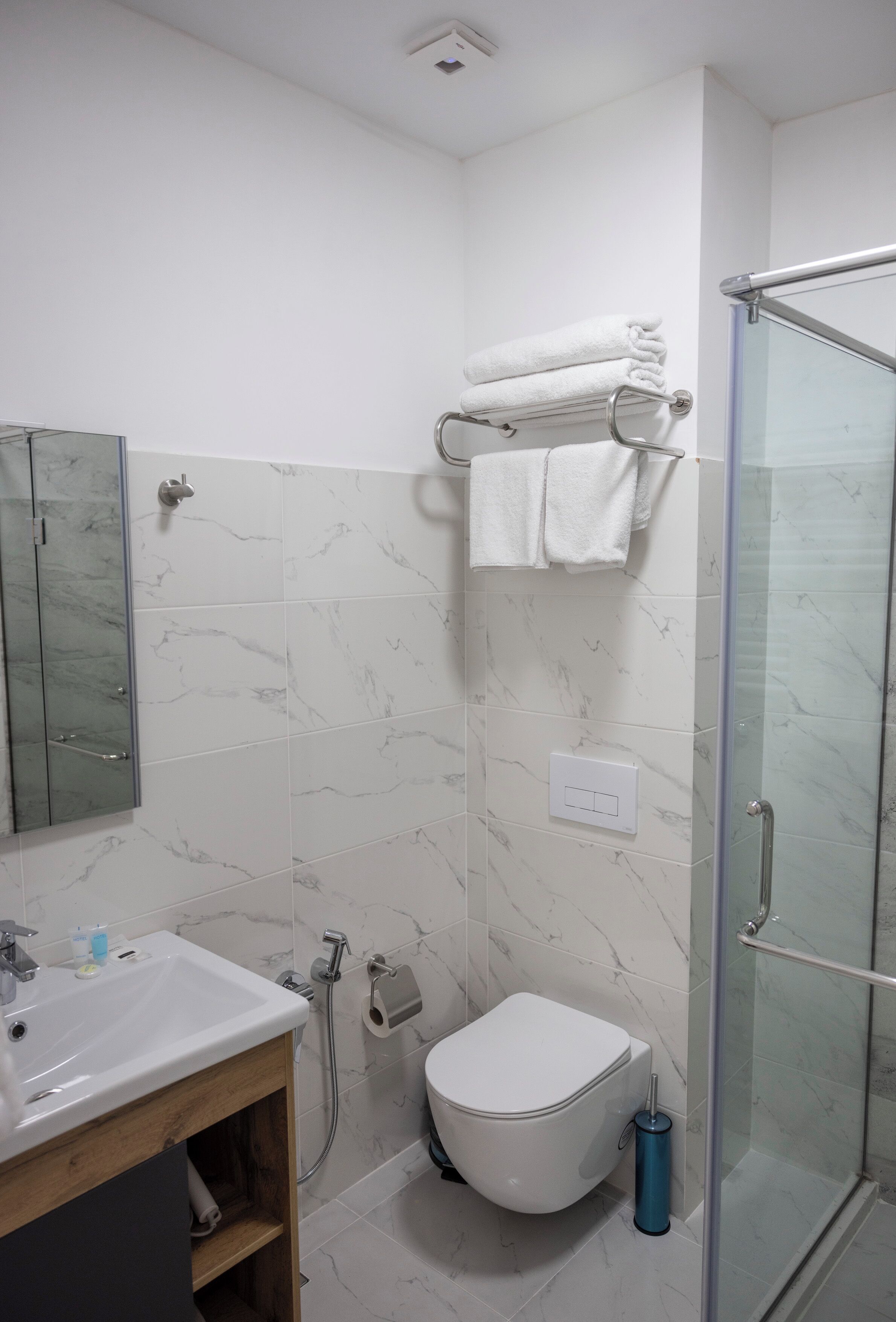 A modern bathroom with a glass shower enclosure, a white toilet, and a marble-tiled wall.