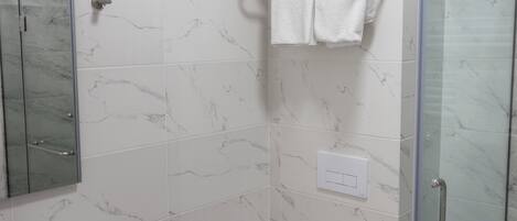 A modern bathroom with a glass shower enclosure, a white toilet, and a marble-tiled wall.