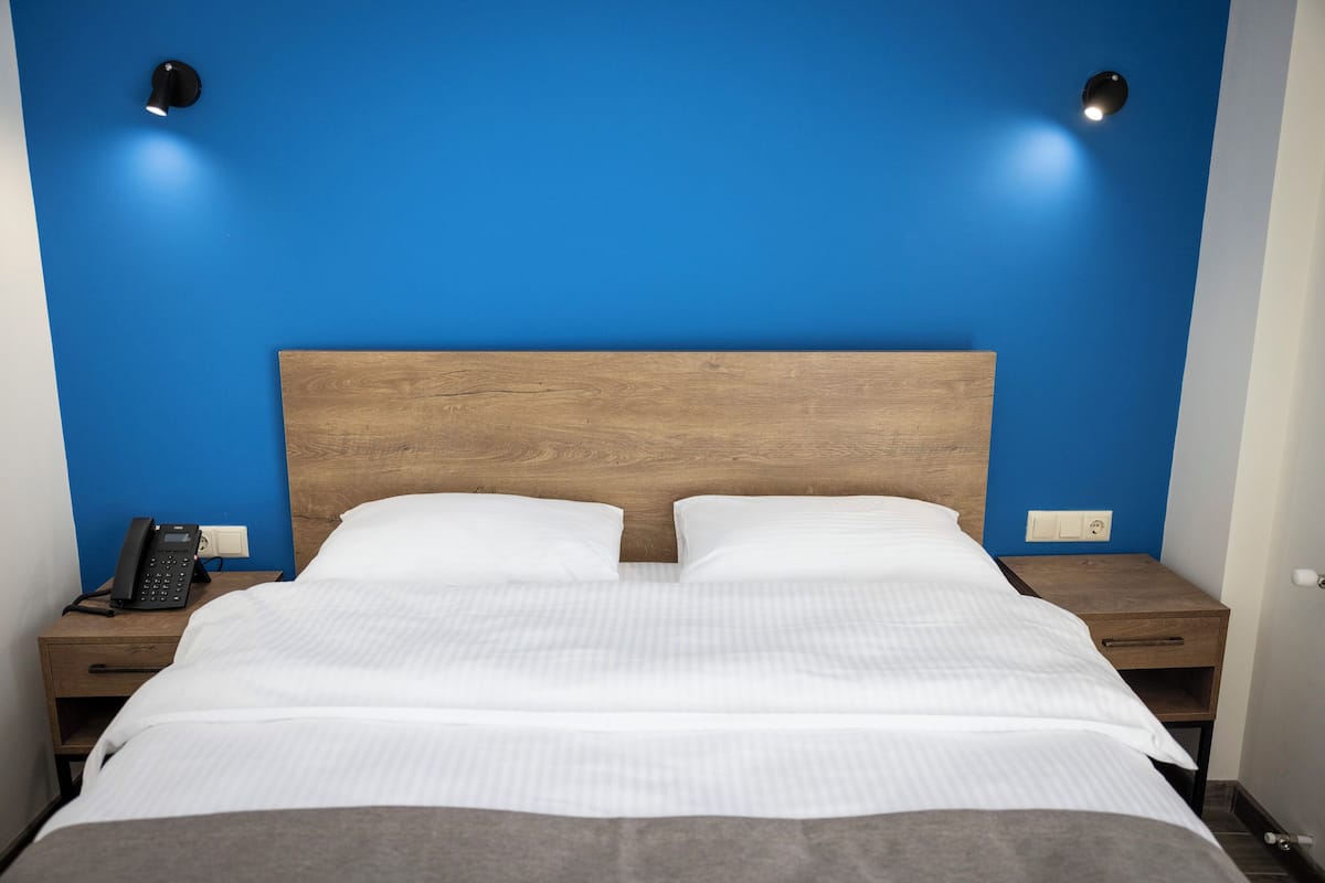 Una cama bien hecha con sábanas blancas, un cabecero de madera y dos mesitas de noche, cada una con un teléfono y una lámpara.