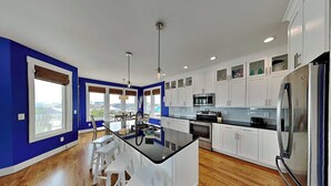 A modern kitchen with white cabinets, a black countertop, and a stainless steel refrigerator. - Shore Sounds Fun | Beach Views + Pet Friendly! (Surf City)