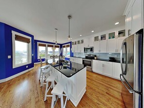 A modern kitchen with white cabinets, a black countertop, and a stainless steel refrigerator. - Shore Sounds Fun | Beach Views + Pet Friendly! (Surf City)