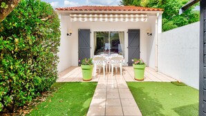 A patio area with a table and chairs, surrounded by potted plants and a white wall.