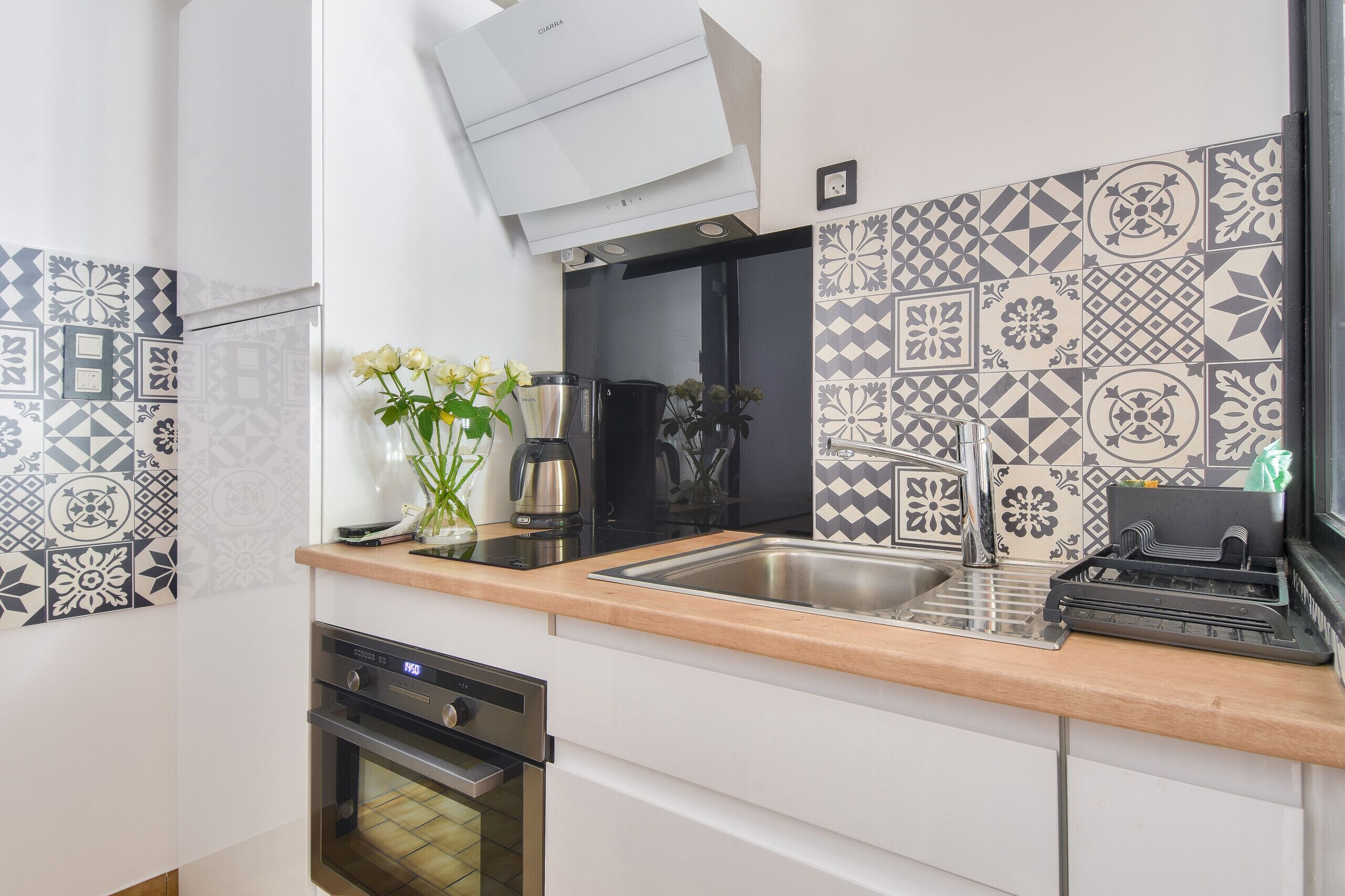 Une cuisine moderne avec des carreaux décoratifs, un évier en acier inoxydable, une machine à café et un four encastré.