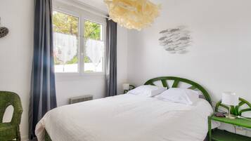Une chambre bien rangée, avec un lit, une chaise, une table de chevet et une fenêtre avec des rideaux.