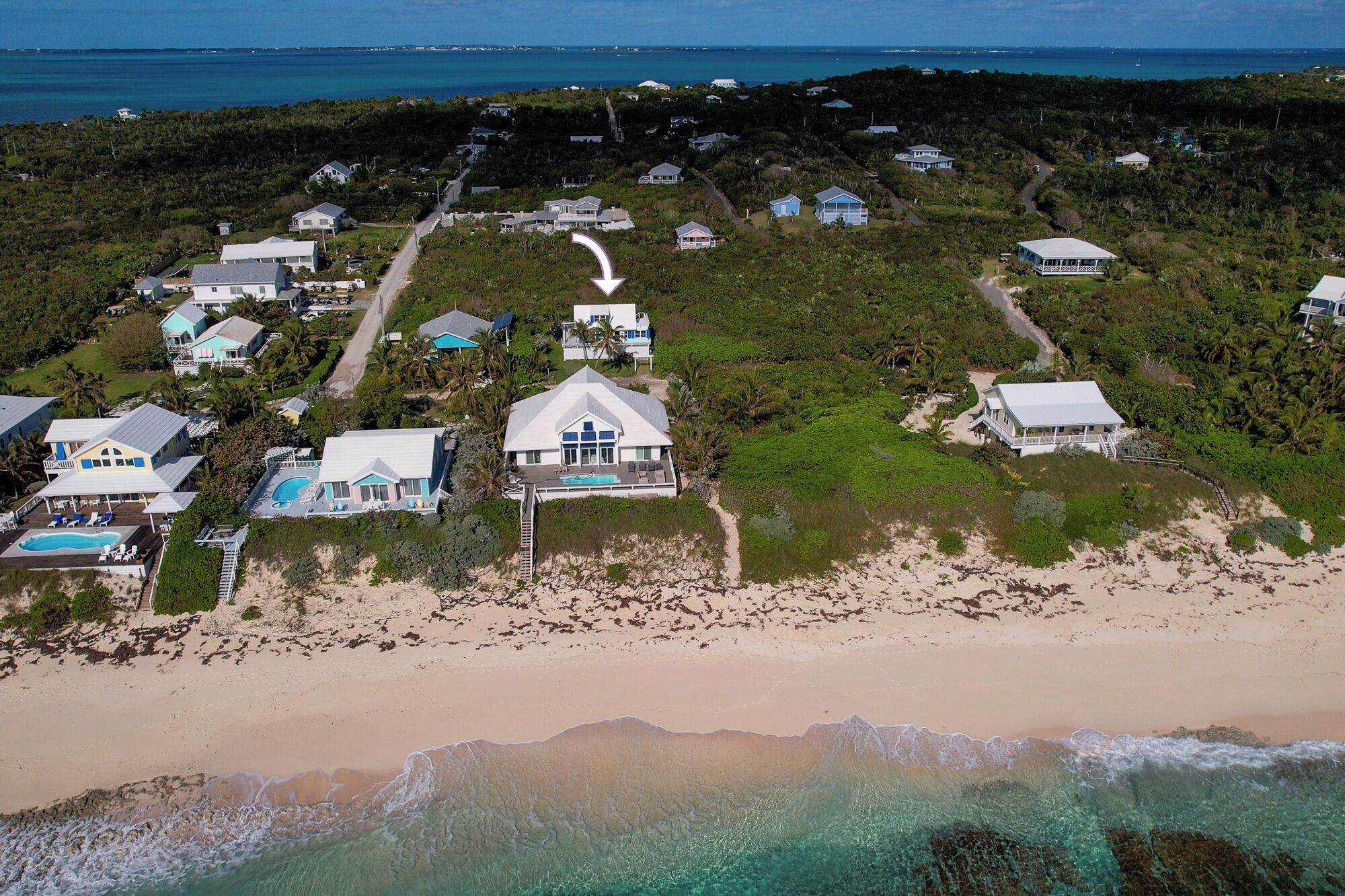 An aerial view of a coastal residential area with houses, a swimming pool, and a beach.