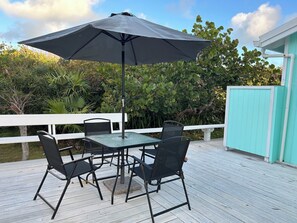 Eine Terrasse mit einem Glastisch, vier Stühlen, einem Sonnenschirm und einem weißen Geländer.