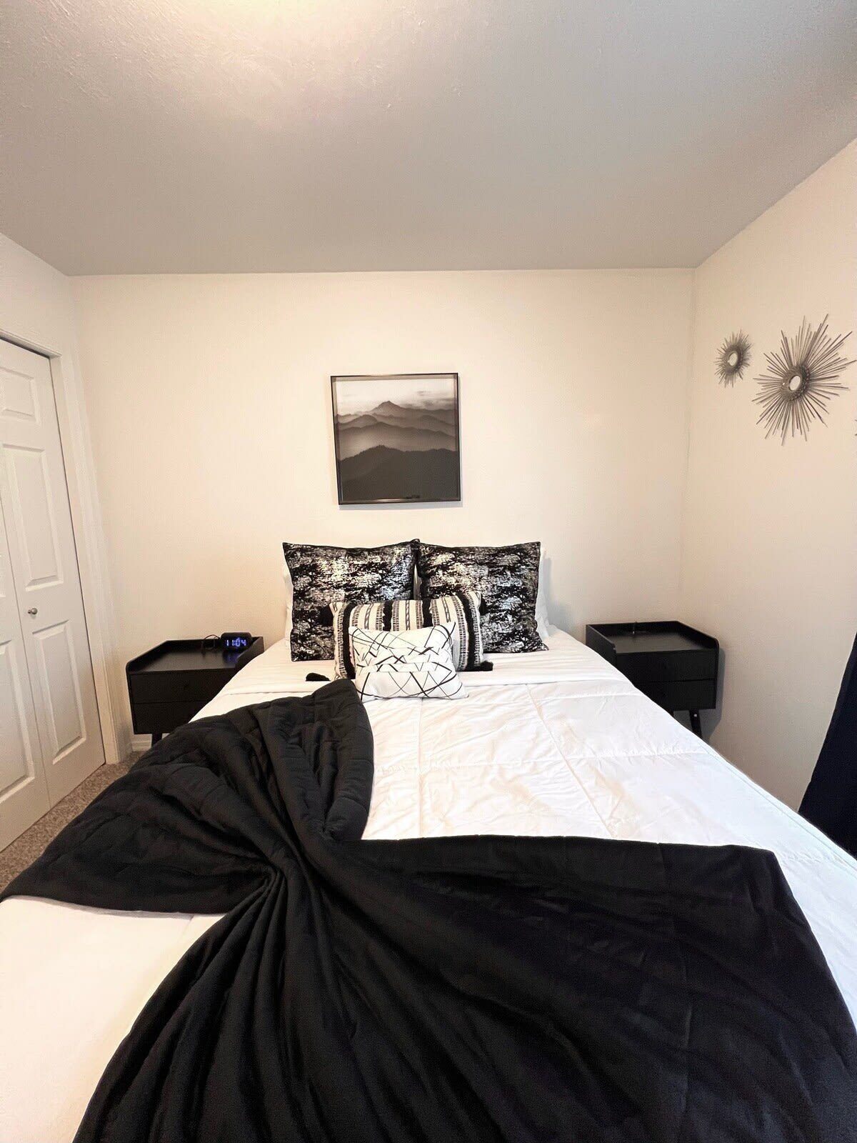 A bedroom with a bed, a bedside table, a nightstand, a wall clock, and a framed picture.
