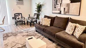 A modern living room with a brown sofa, patterned cushions, a white coffee table, and a large abstract painting on the wall. - Modern & Stylish, King bed, WiFi (Spokane Valley)