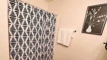 A bathroom with a bathtub, a shower curtain with a black and white pattern, a white towel on the wall, and a framed picture of a vase with flowers.