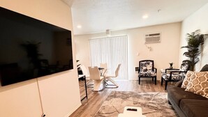A modern living room with a flat-screen TV mounted on the wall, a brown sofa, a patterned armchair, and a coffee table. - Modern & Stylish, King bed, WiFi (Spokane Valley)