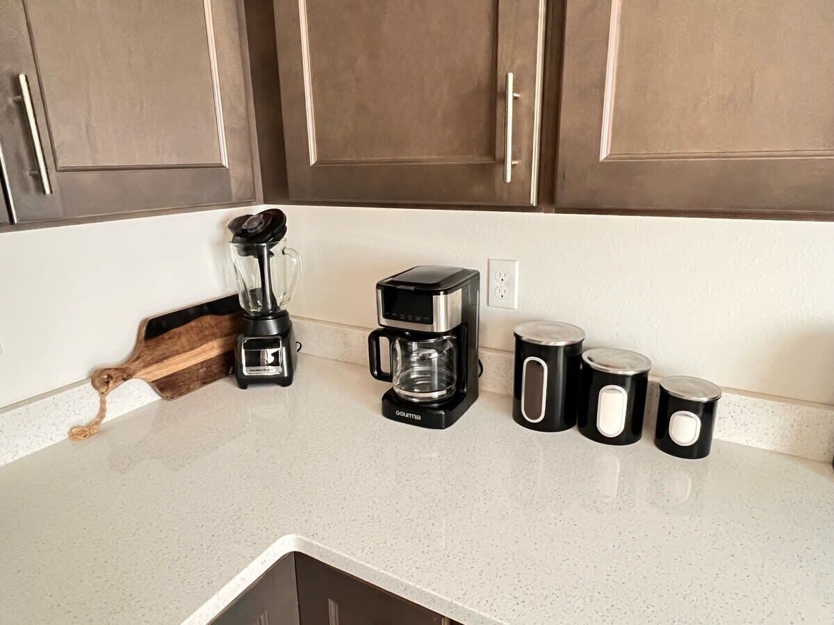 A kitchen counter with a coffee maker, a blender, and three black mugs.