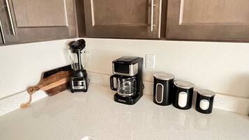 A kitchen counter with a coffee maker, a blender, and three black mugs.
