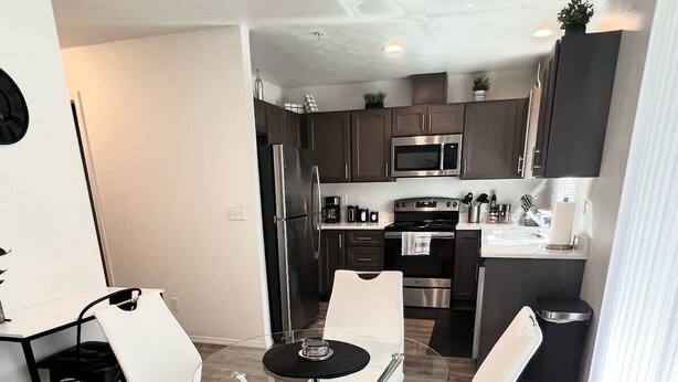 A modern kitchen with stainless steel appliances, a dining area with white chairs and a glass table, and a wooden floor. - Modern & Stylish, King bed, WiFi (Spokane Valley)