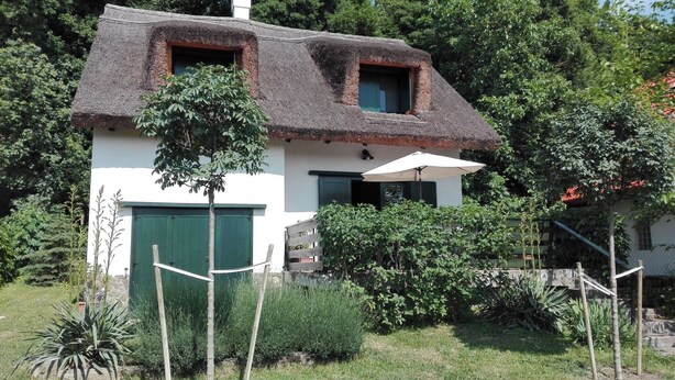 Ein traditionelles Haus mit einem Reetdach, einer grünen Tür und einer kleinen Veranda mit einem weißen Sonnenschirm.