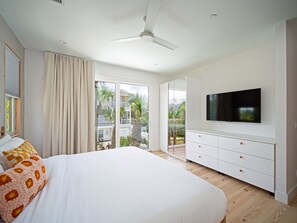 A bedroom with a bed, a TV, a ceiling fan, and a sliding glass door leading to a balcony. - 2 Heated Pools | Ocean Views | Sleeps 24 (Jacksonville Beach)