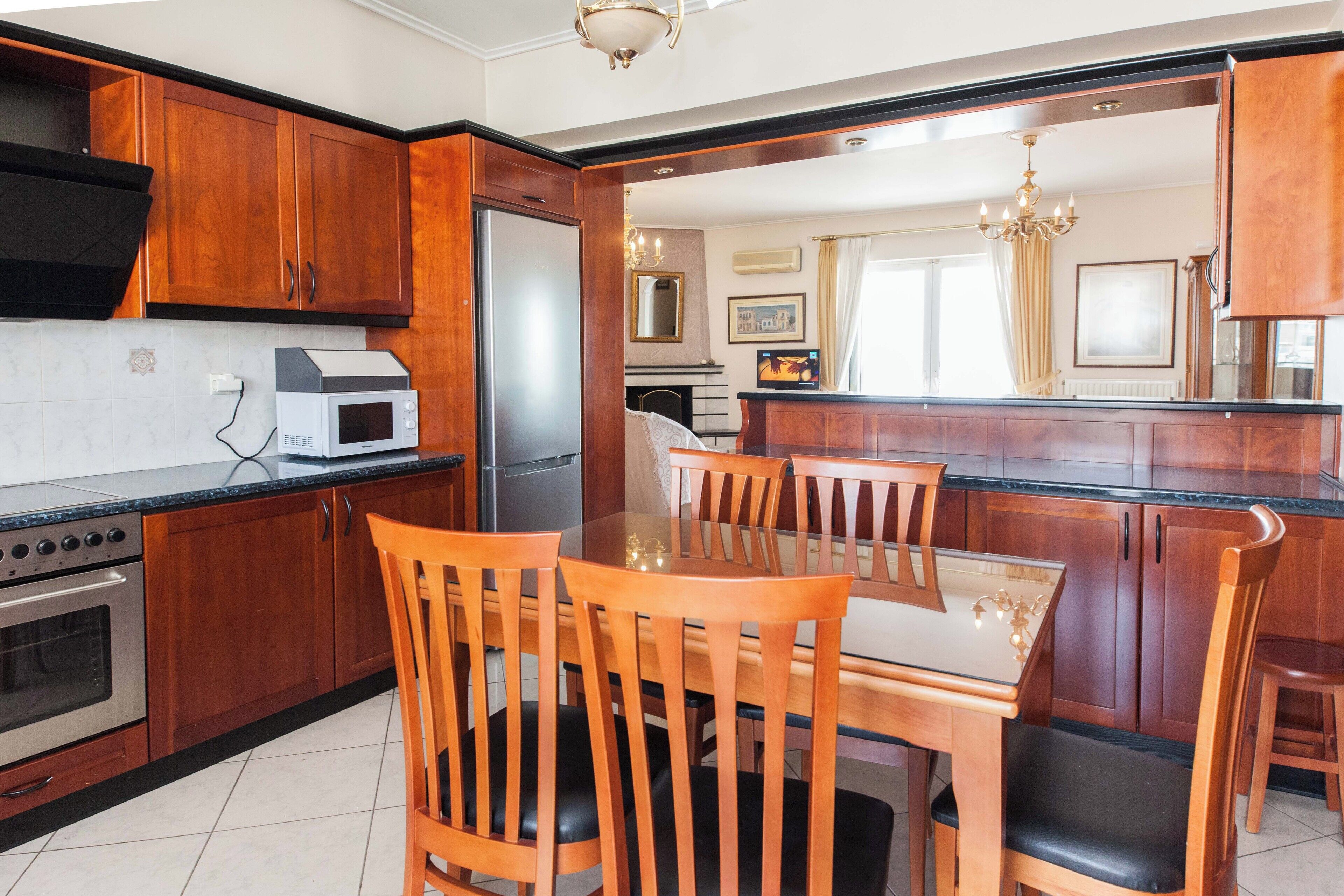 Een moderne keuken met houten kastjes, een inbouwmagneetronoven en een eethoek met een glazen tafel en houten stoelen.