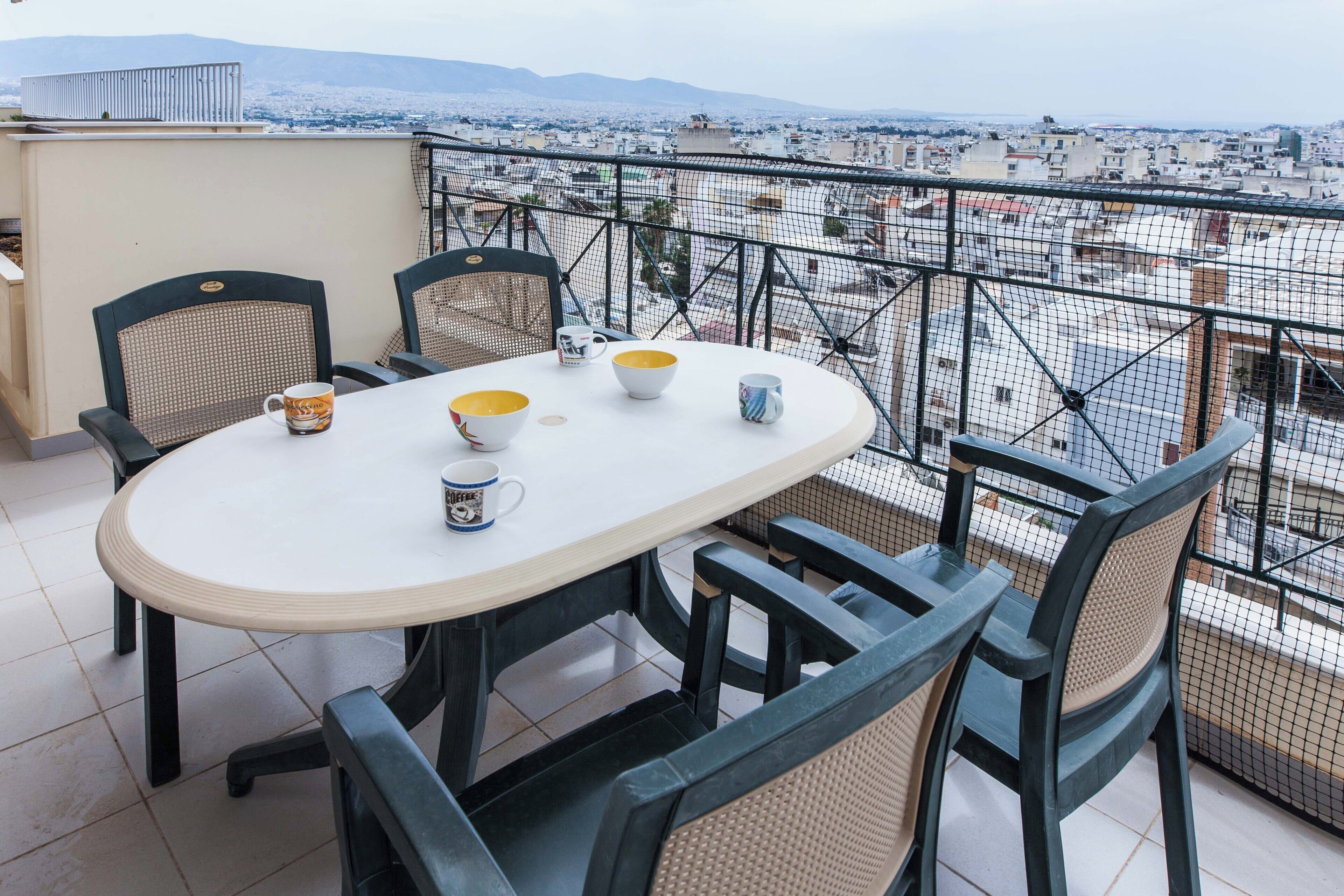 Uma mesa redonda com cadeiras e vista para a cidade através da grade da varanda.